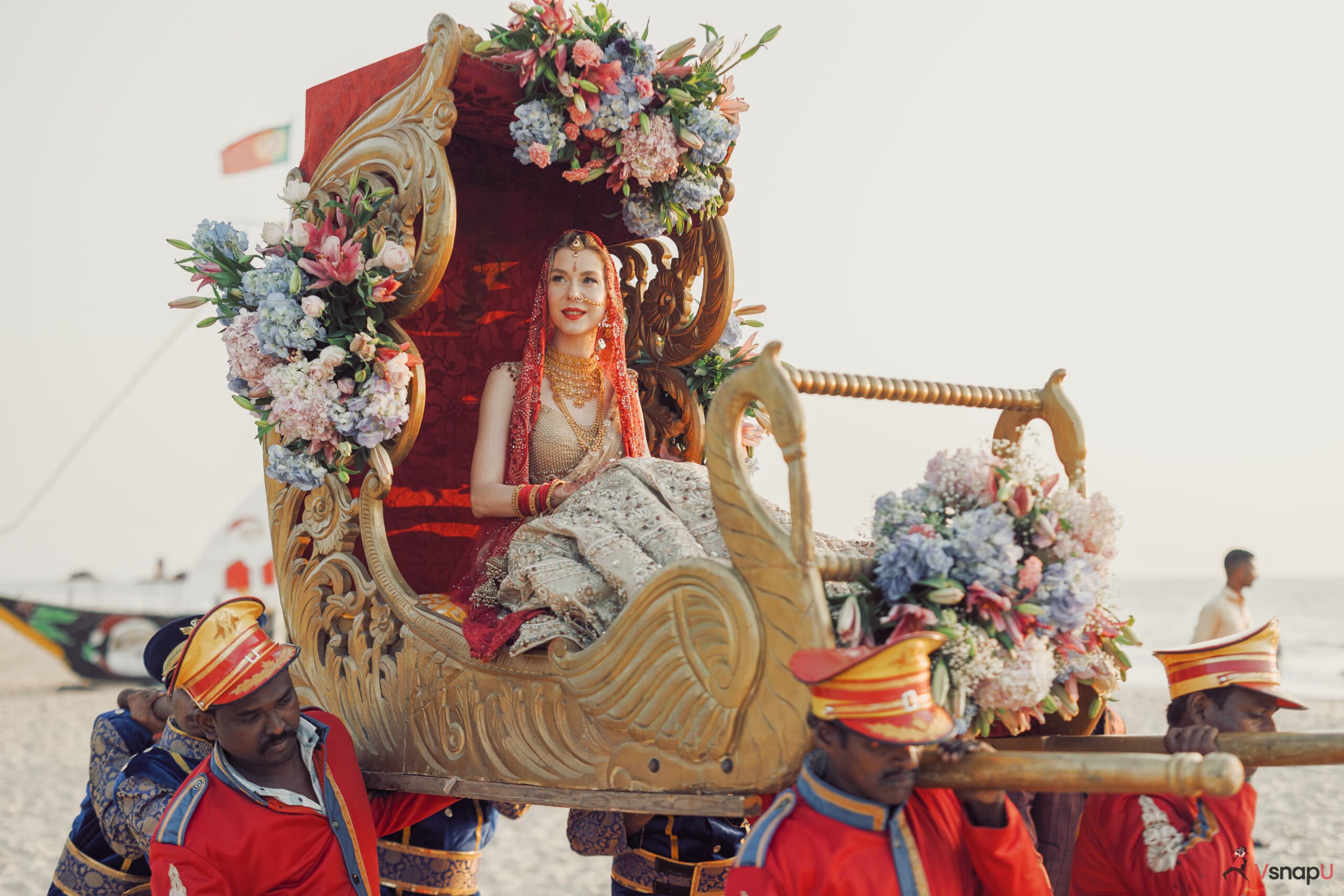 The bride beams with joy, sitting in her wedding doli by the serene seaside.